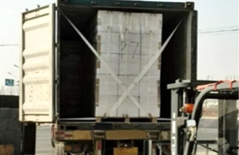 Cargo secured inside an open shipping container with crossed white lashing straps.